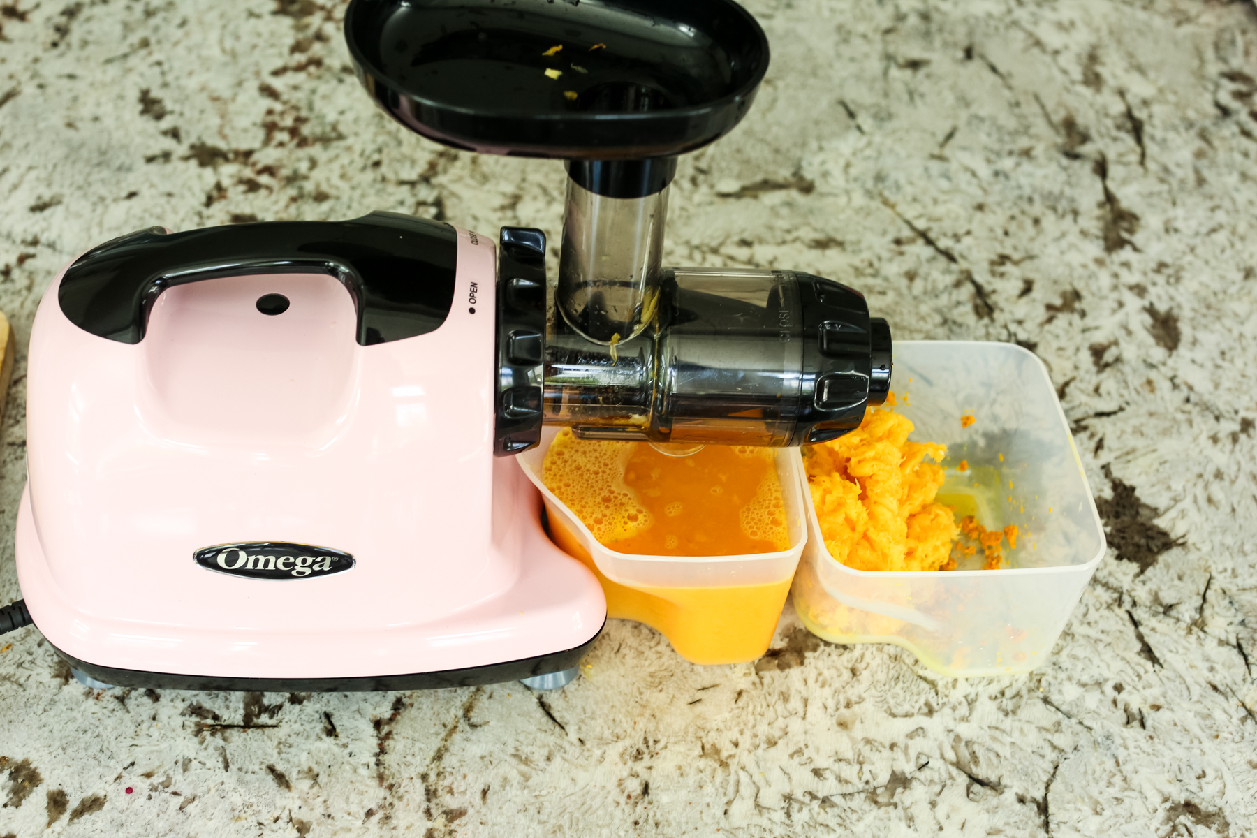 a pink juicer extracting orange liquid