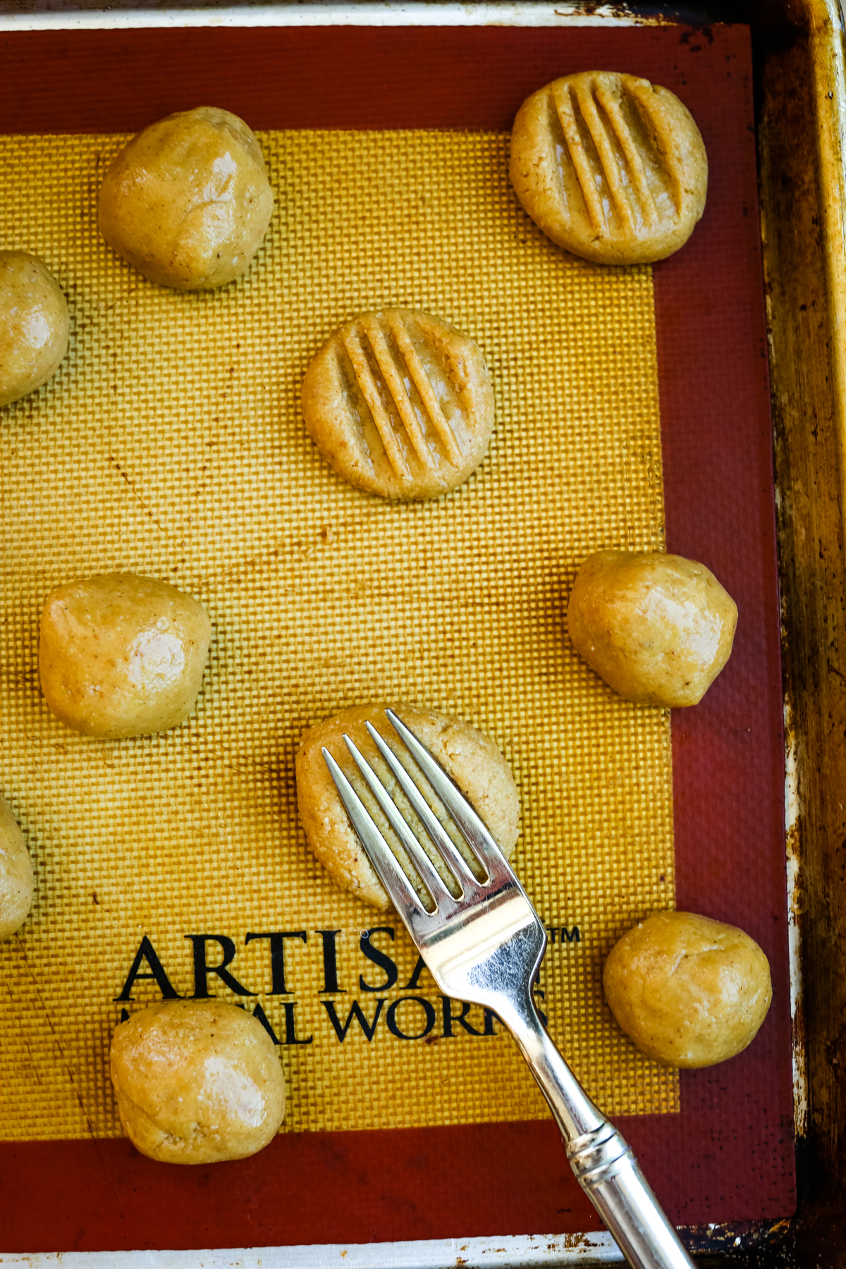 raw cookies on a baking sheet with a fork adding a crisscross pattern