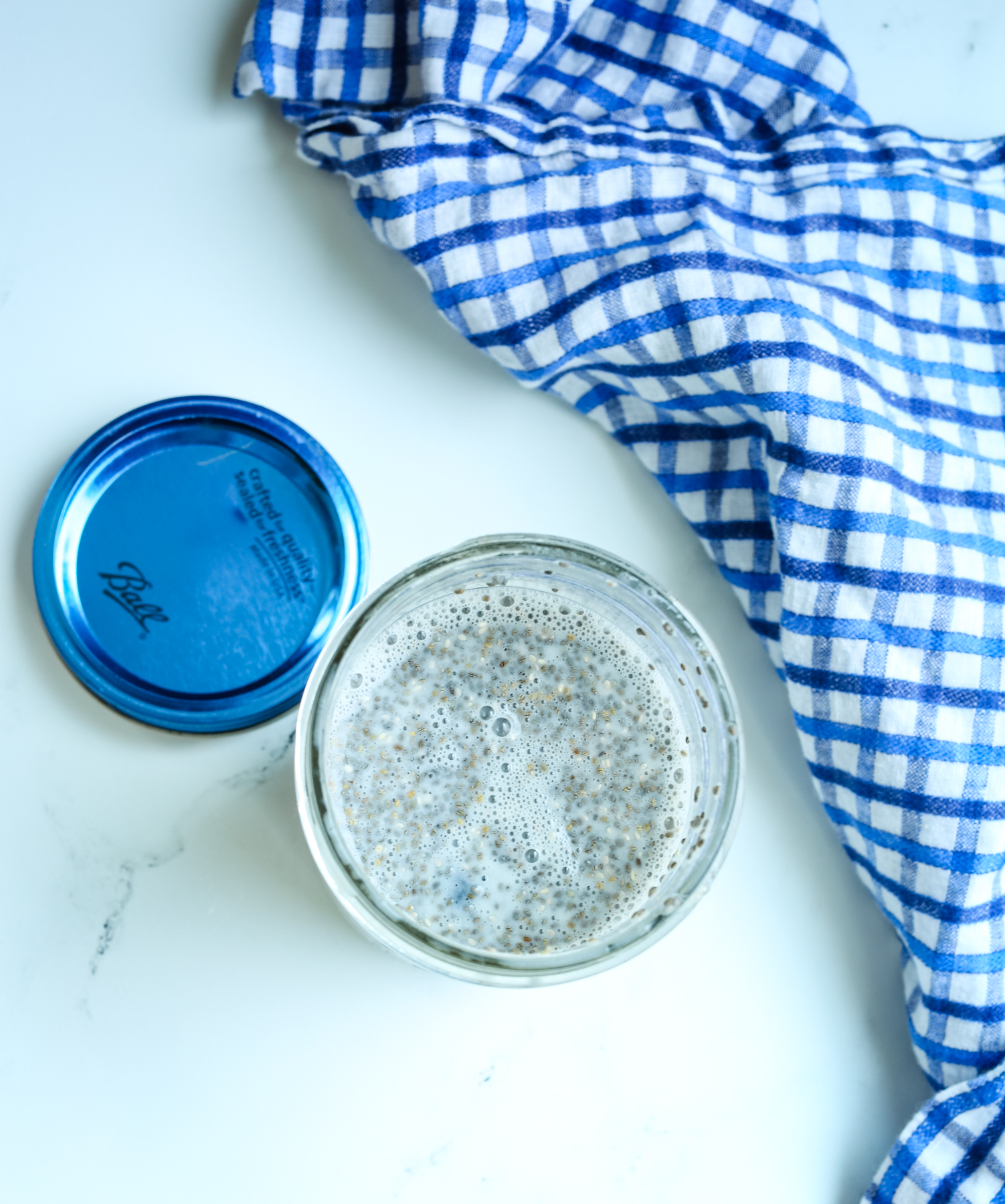 overhead shot of a mason jar with milk and chia seeds and a blue checked napkin