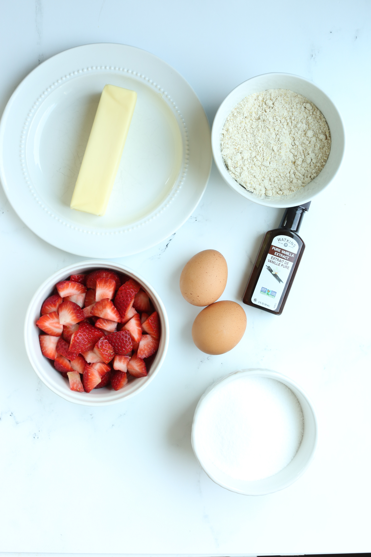 recipe ingredients overhead shot: butter, flour, strawberries, eggs, erythritol, and vanilla extract 