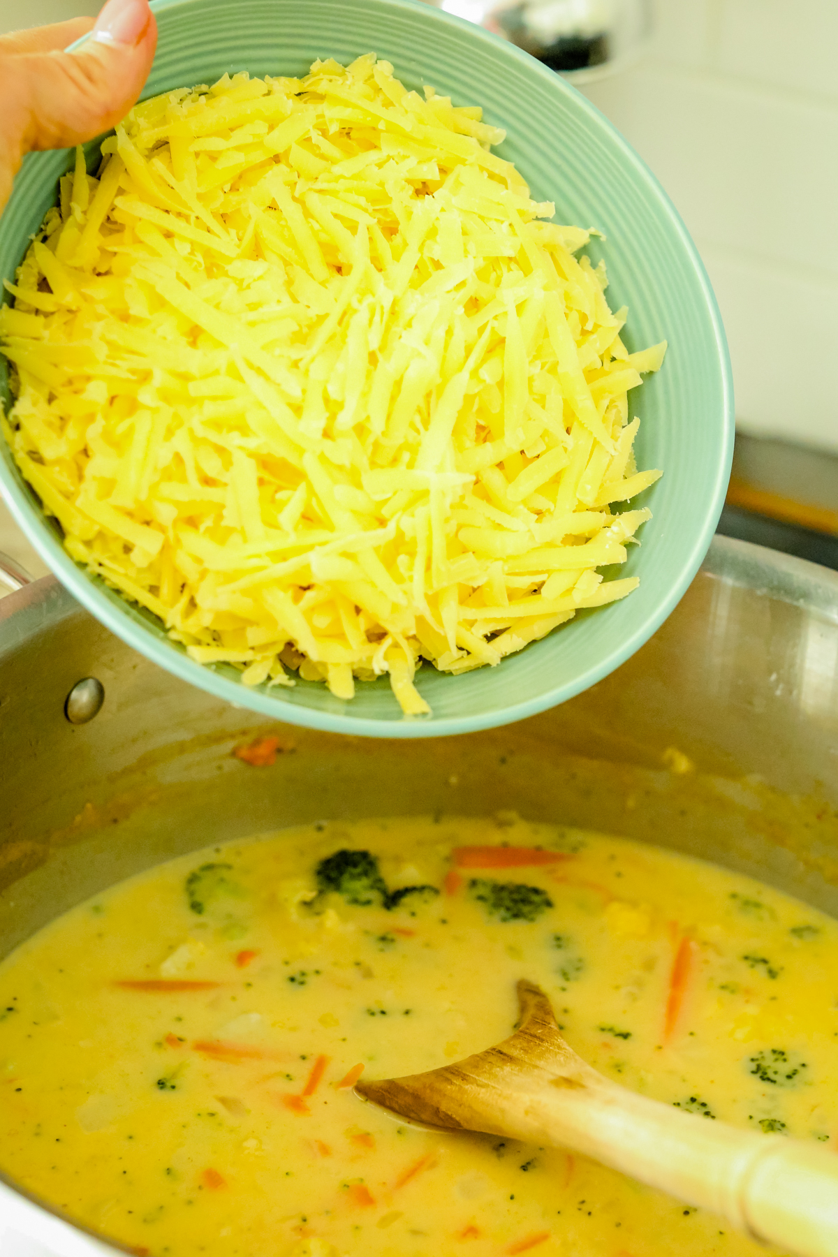 pouring shredded cheese into a pot of soup