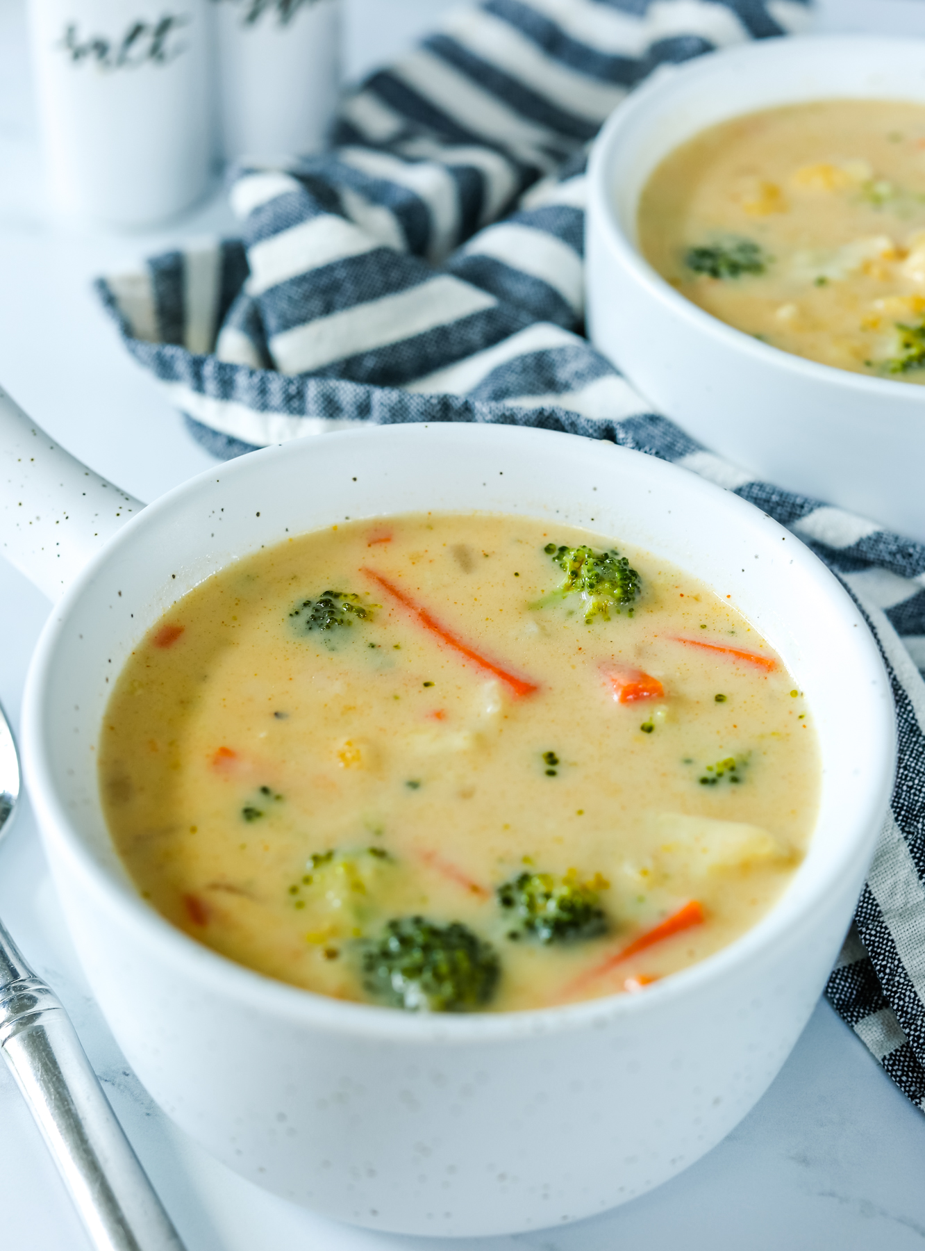 a bowl of broccoli cauliflower soup with a striped napkin and second bowl in the background