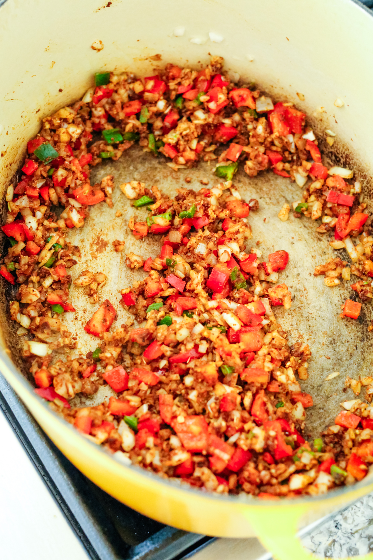 onions and peppers being sautéed in oil in a Dutch oven 