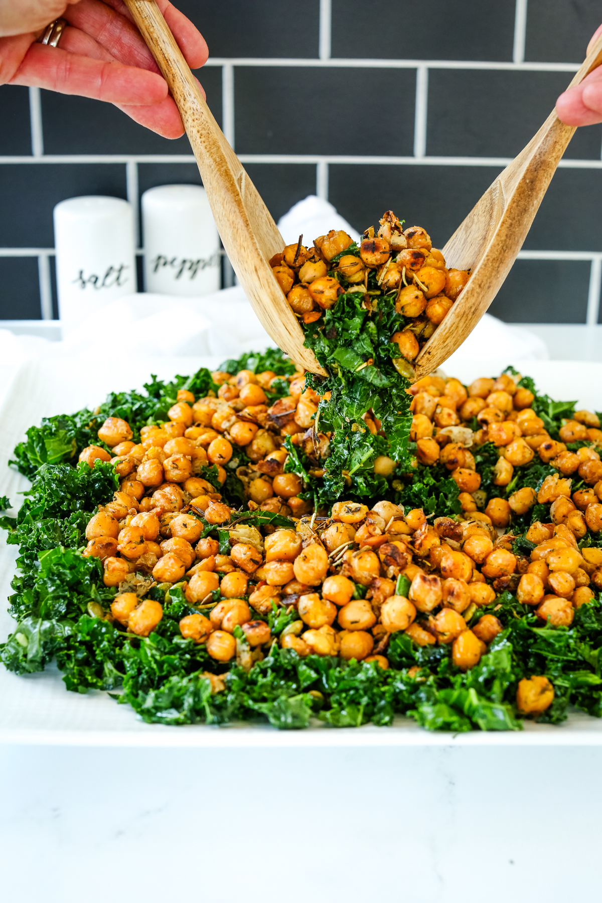 a plate of crispy chickpeas and kale with tongs lifting the salad