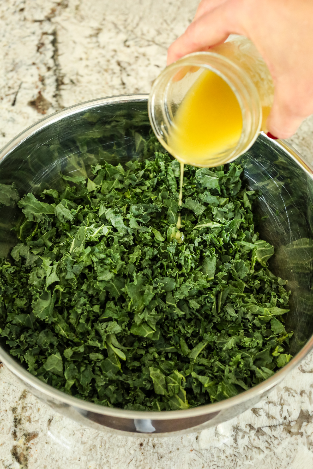 pouring a yellow hued dressing over chopped kale