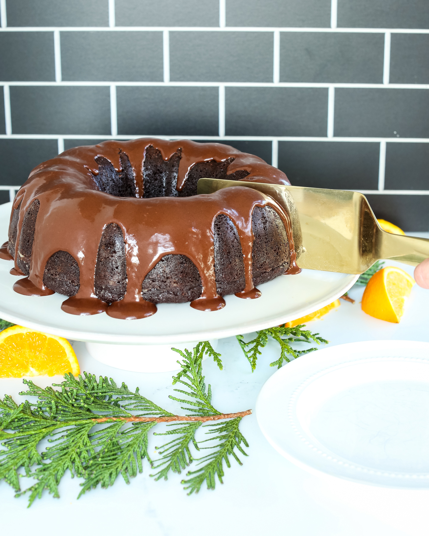 a beautiful chocolate cake on a white platter with greenery and oranges