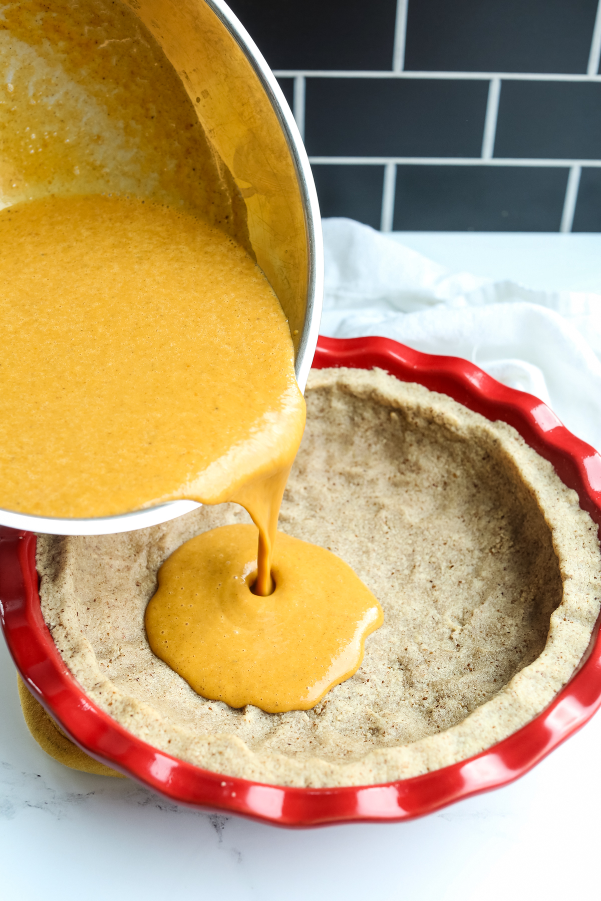 pouring a pumpkin pie filling into a crust