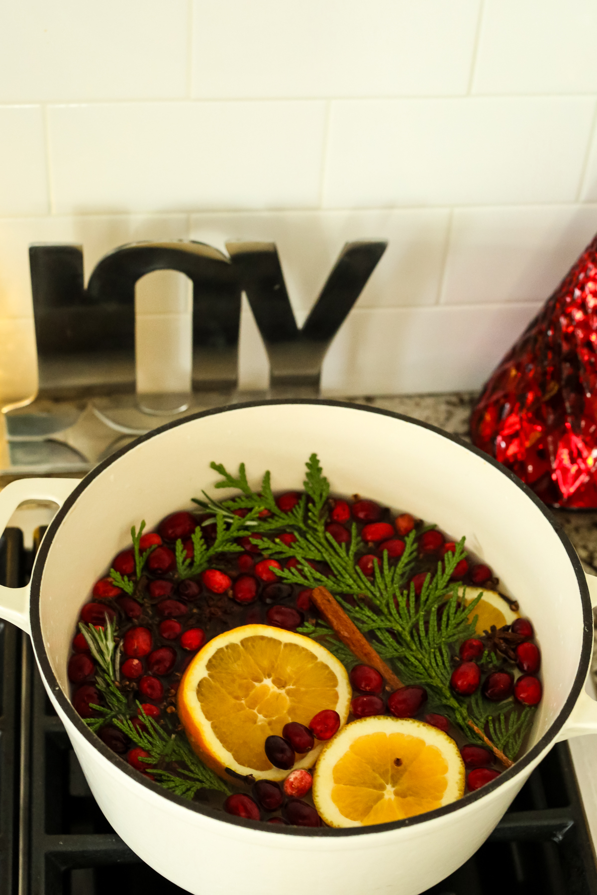 a cream colored pot of oranges, evergreen cutting, and cranberries on a stove top