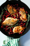 cranberry chicken in a cast iron skillet surrounded by fresh rosemary