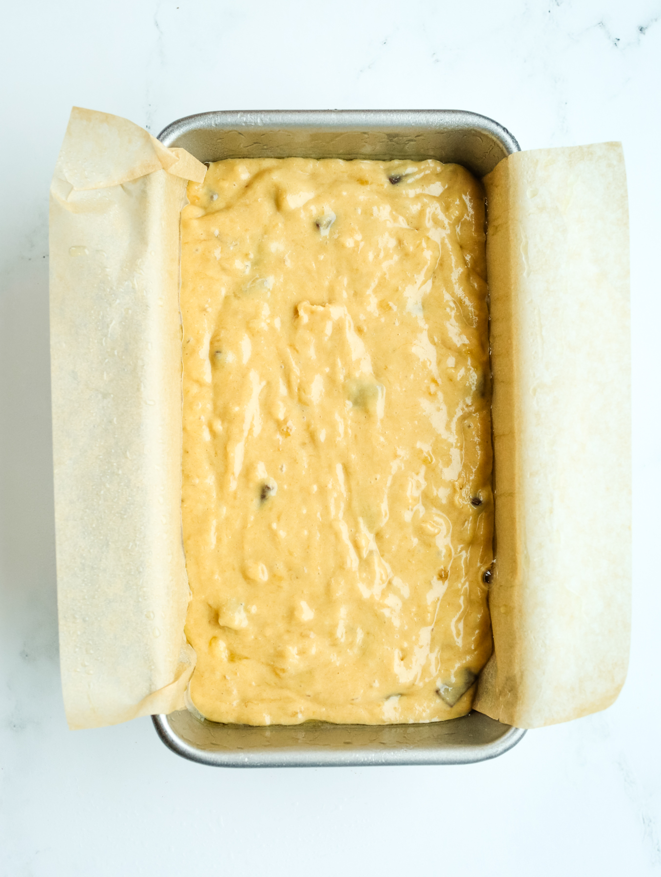 raw banana bread batter in a loaf pan with parchment paper 