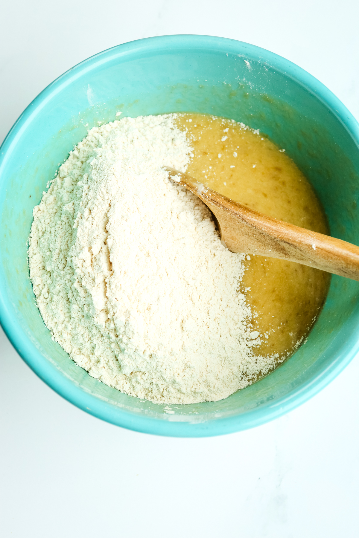 adding dry ingredients to wet ingredients in the blue bowl 