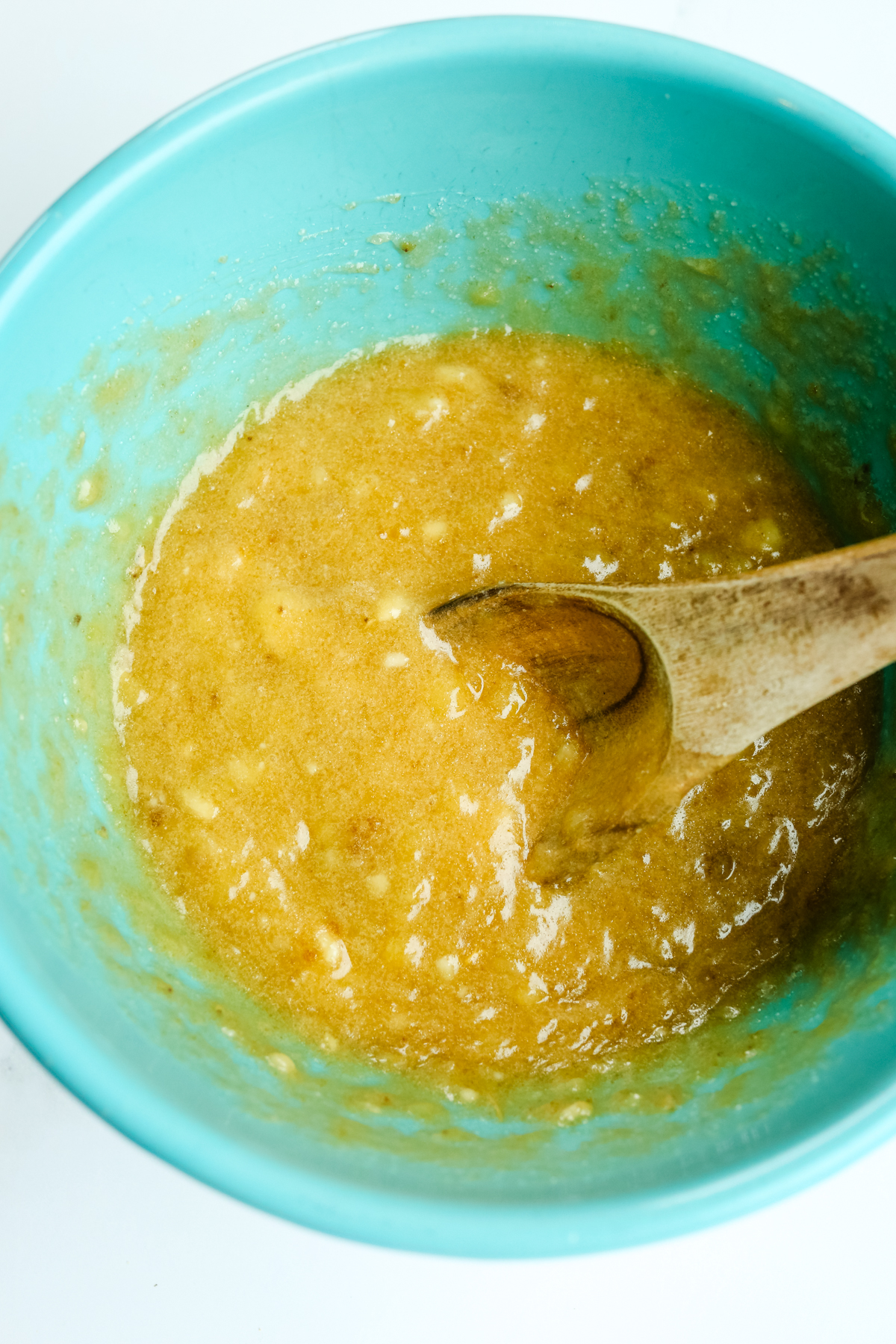 sugar, bananas, and melted butter combined in a blue bowl with a wooden spoon