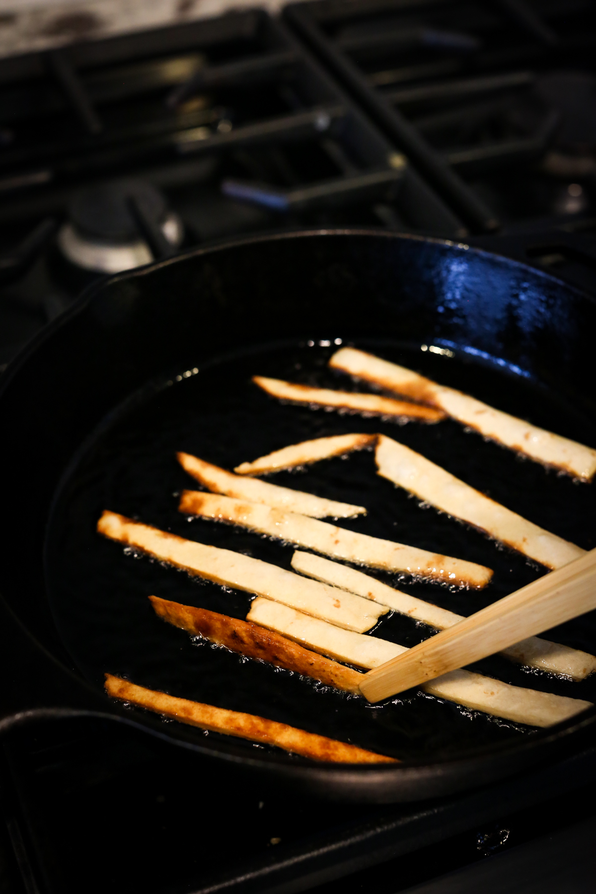 tortilla strips being fried in a cast iron skillet