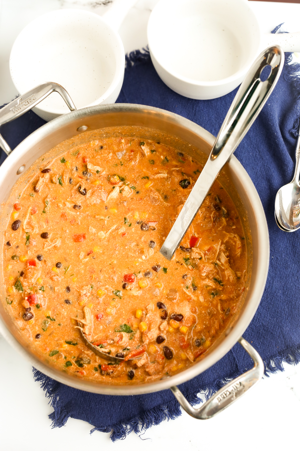 on overhead shot of a big pot of creamy chicken tortilla soup with a ladle in the pot and two empty bowls