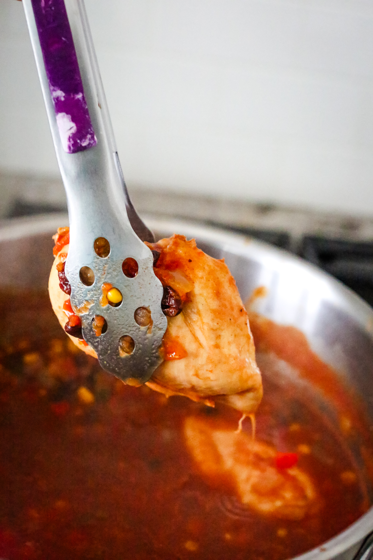 removing a cooked chicken breast from a pot of soup with tongs