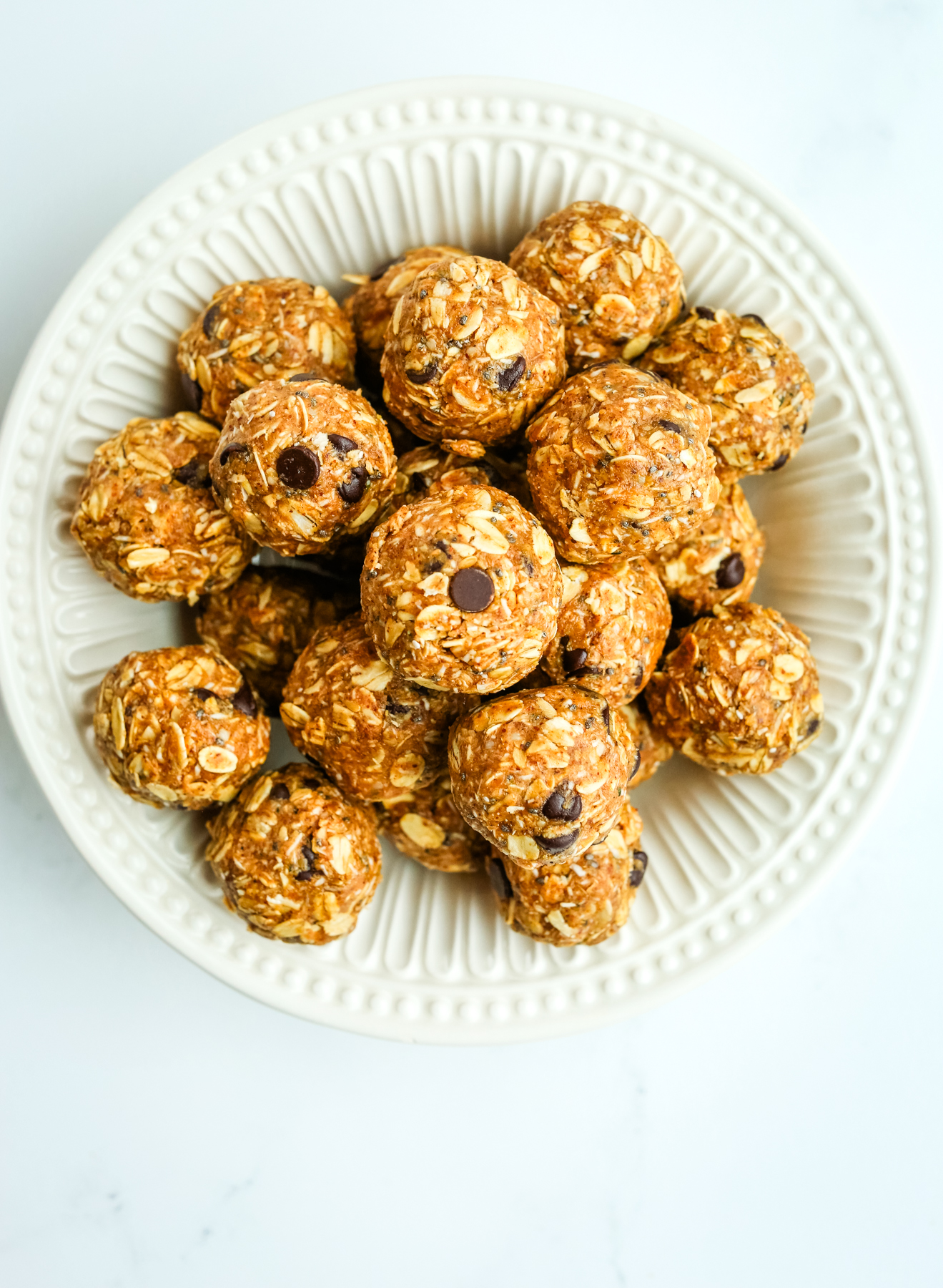 a white bowl on a white counter with oat-based balls with chocolate chips in them