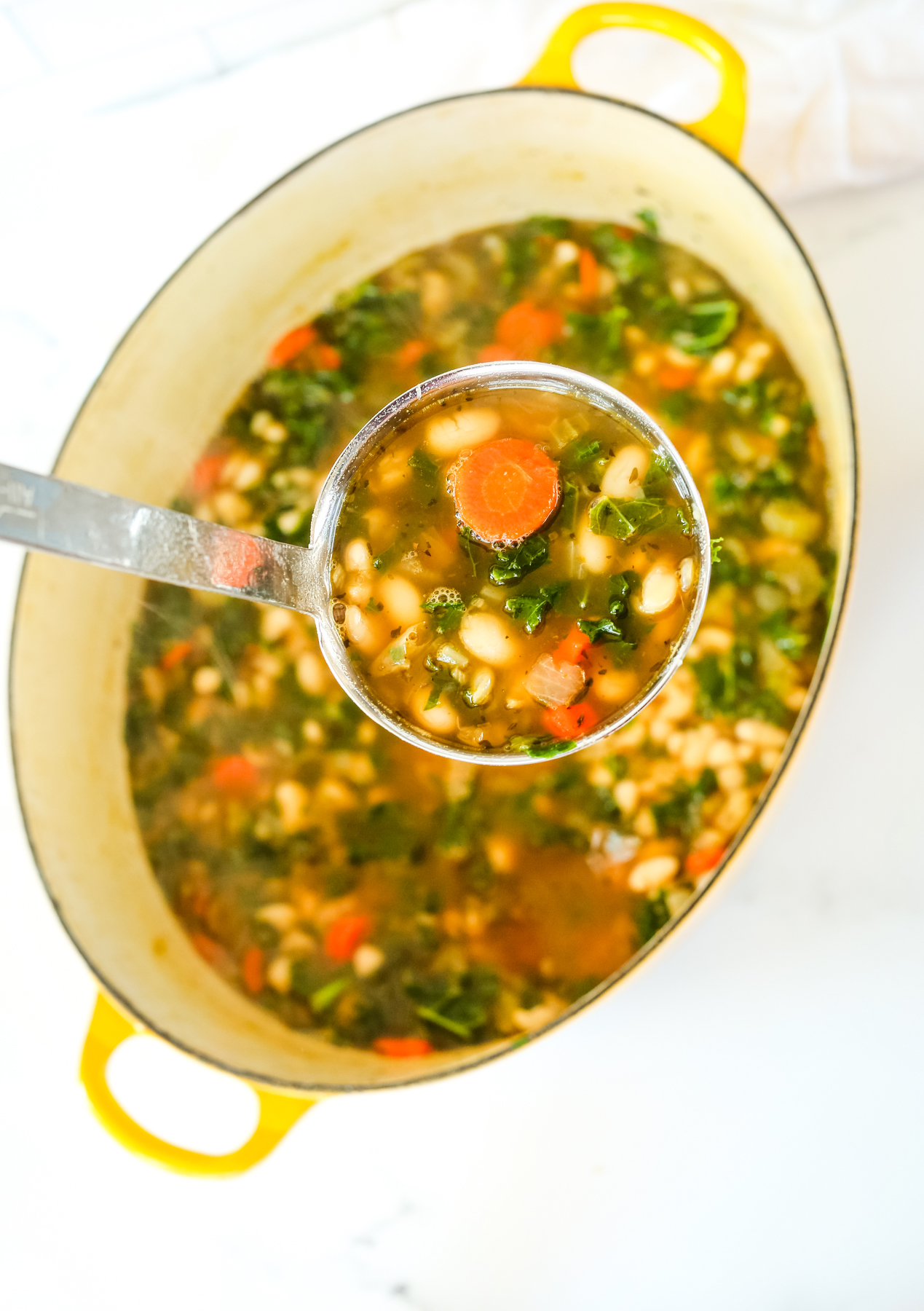 a big pot of white bean soup with a ladle taking a scoop out