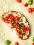 A slice of toast with cottage cheese, quartered grape tomatoes,and strips of basil