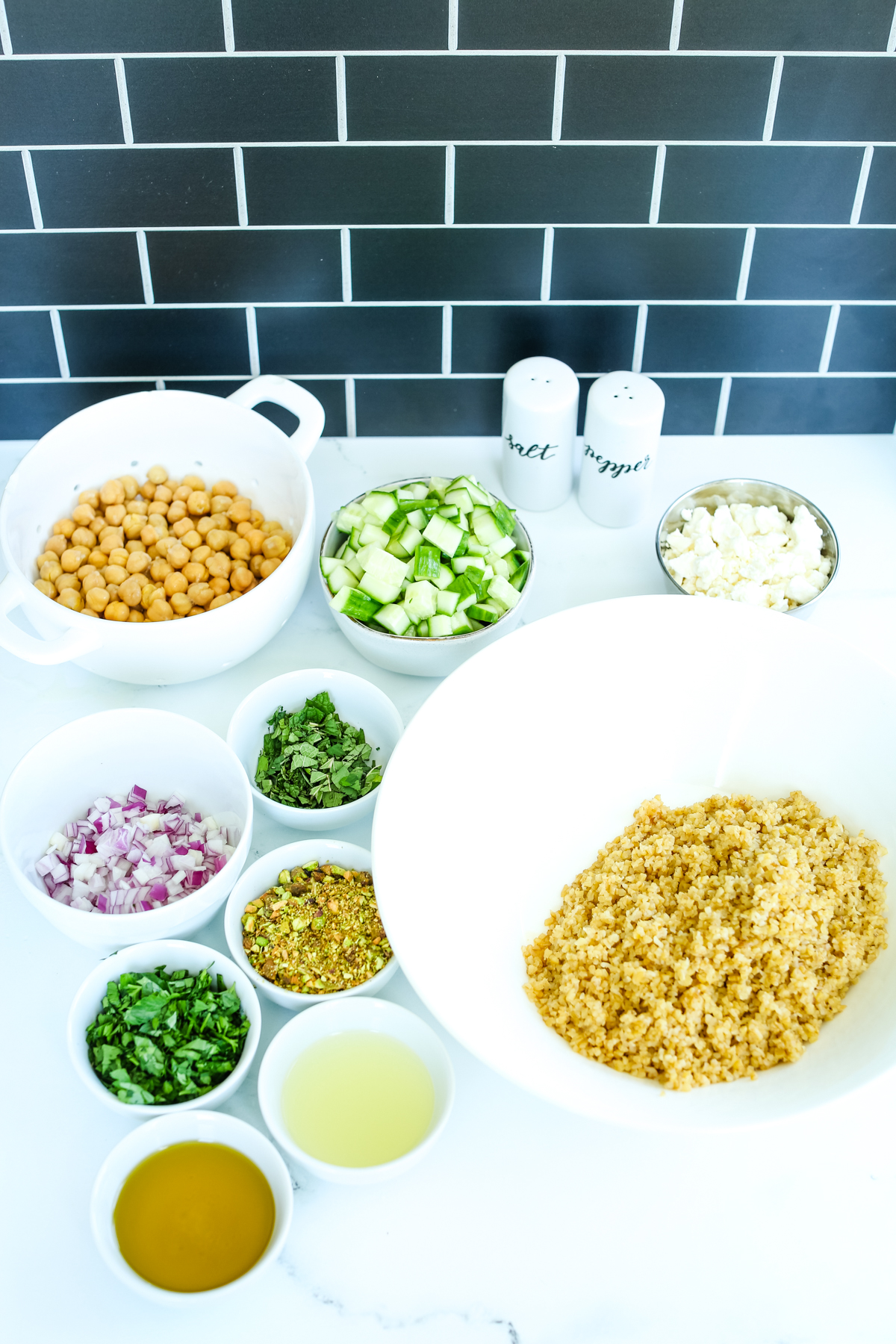 cooked bulgur wheat in a white bowl with the rest of the salad ingredients in small bowls surrounding it