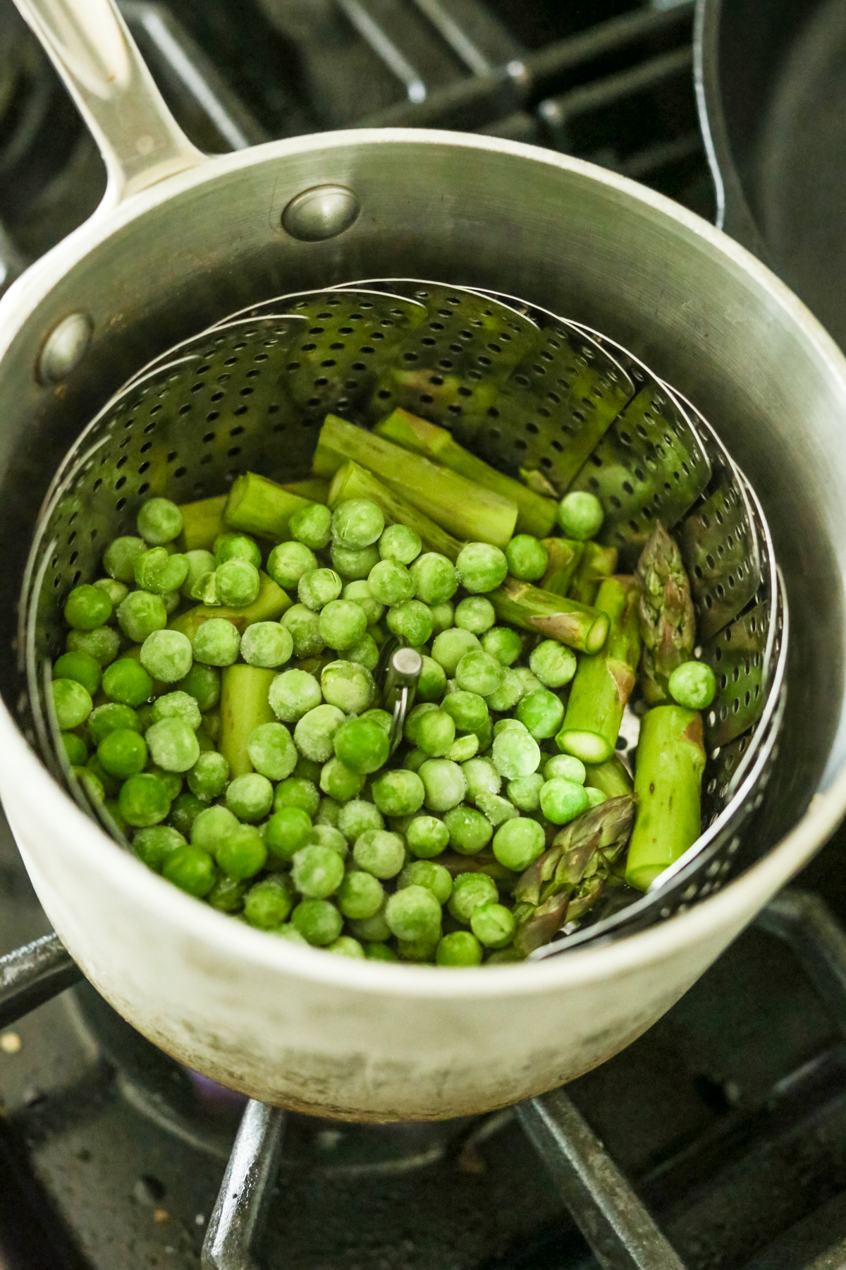 a steamer basket inside a pot with peas and asparagus