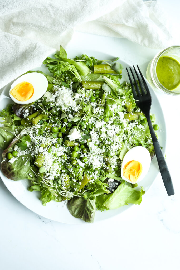 a spring salad with hard boiled eggs on a plate with a black fork and green dressing in a jar