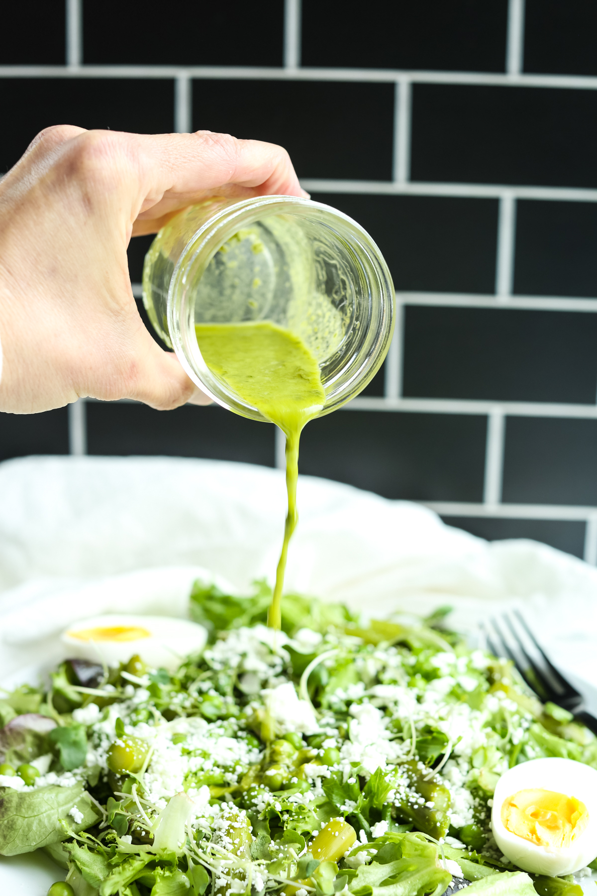pouring green dressing on a plate of spring salad