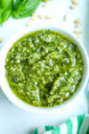 A close up shot of basil pesto recipe in a white bowl