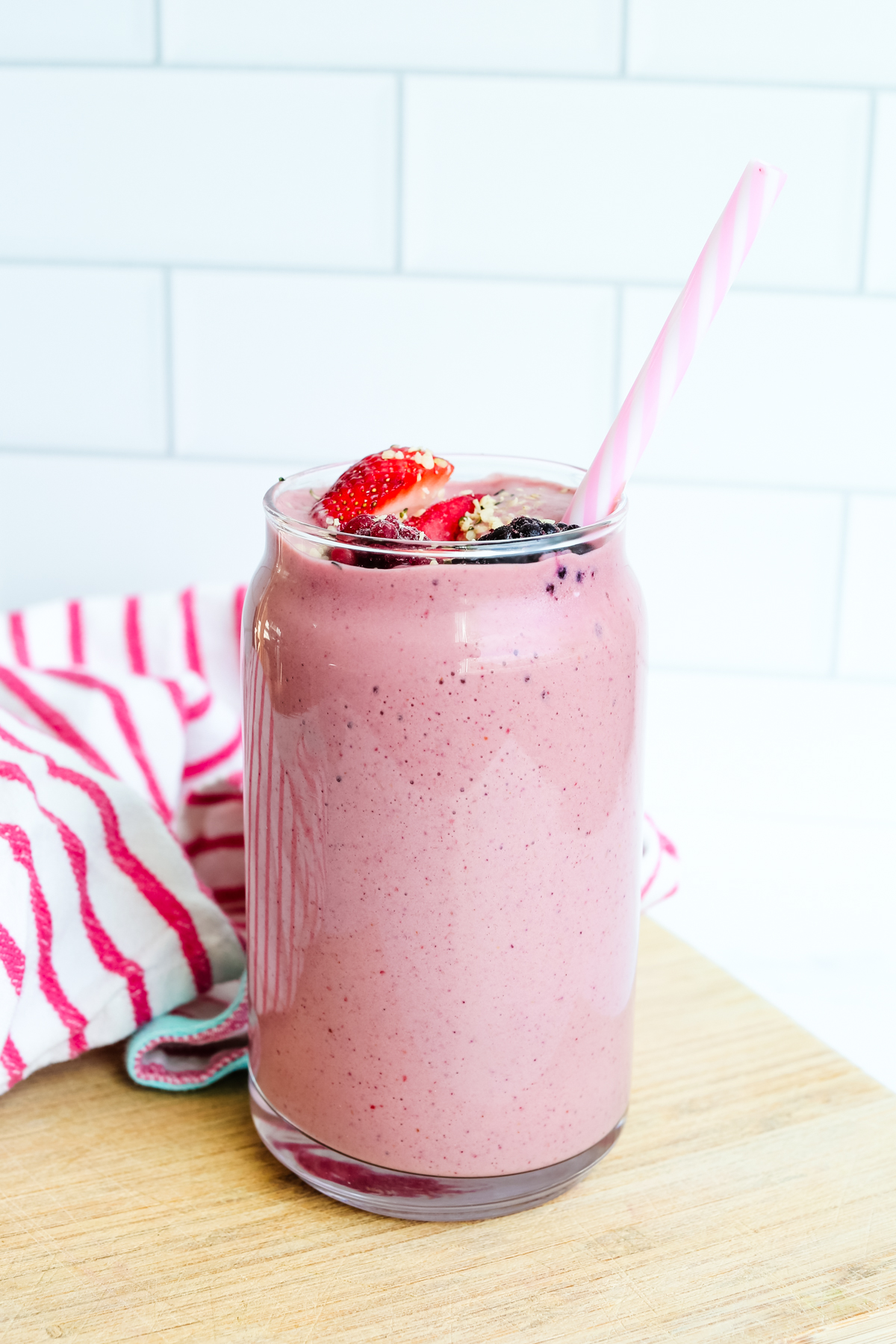 A berry smoothie on a cutting board with a plastic straw
