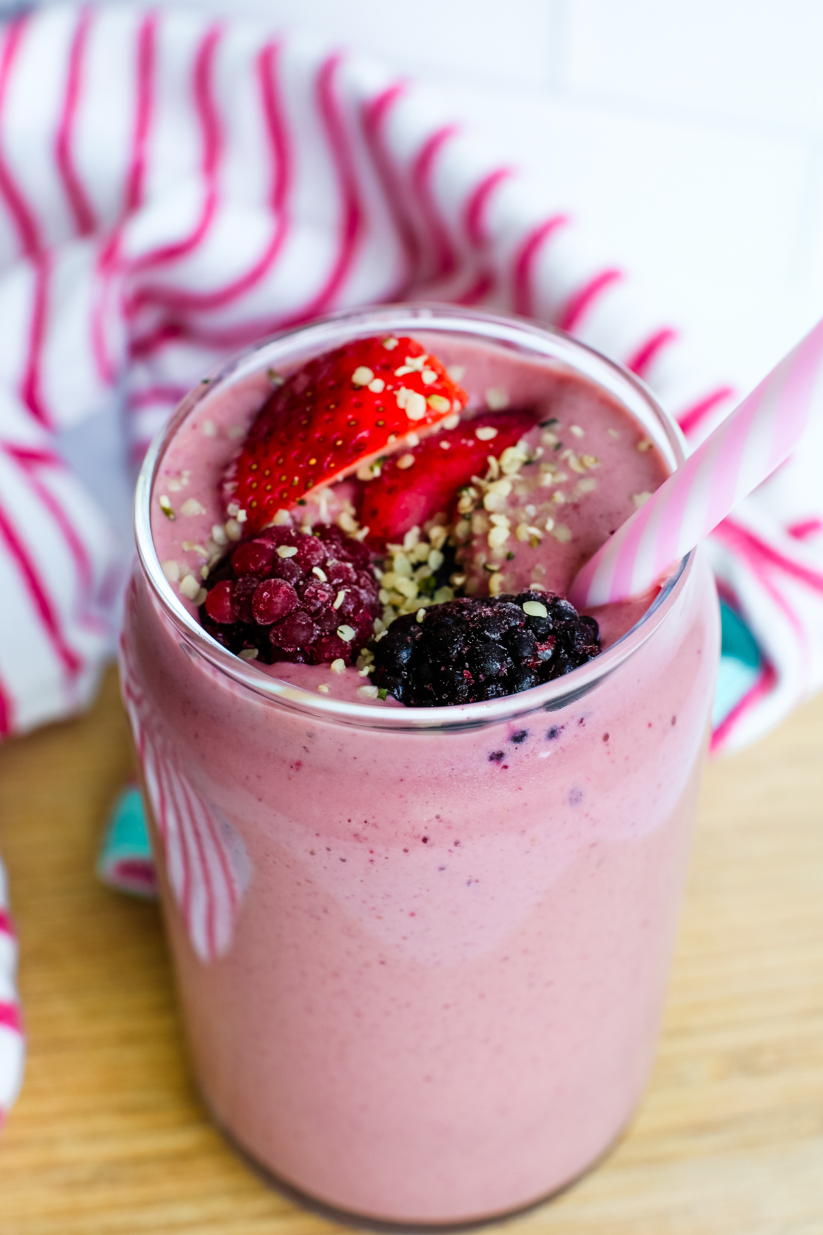 a berry smoothie with a pink and white straw and napkin