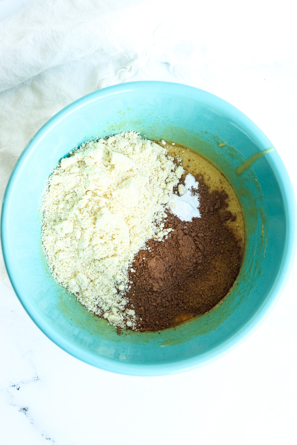 adding dry ingredients to wet ingredients in a turquoise bowl