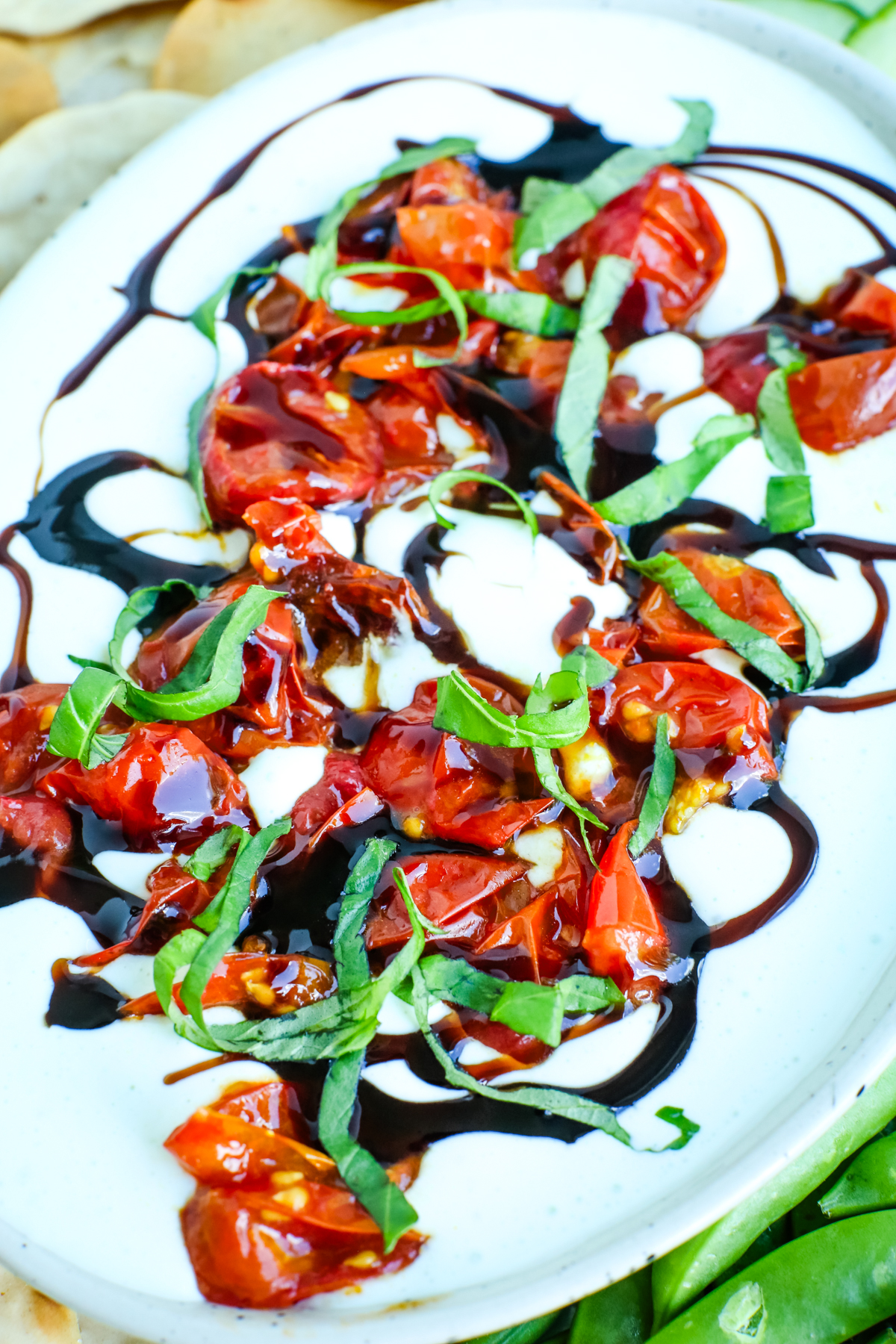 a white dip with tomatoes, fresh basil strips, and a balsamic glaze drizzled on top