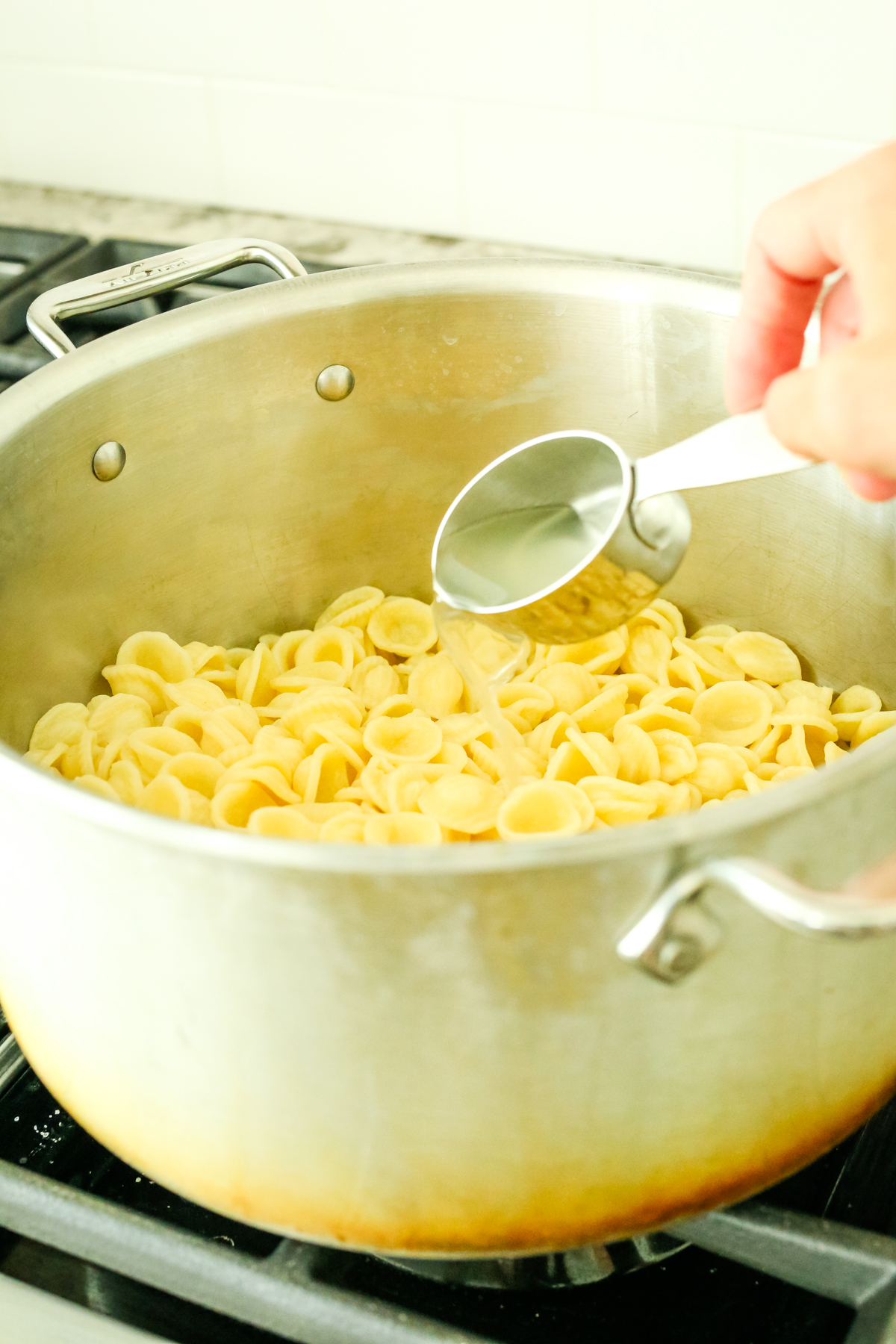 a pot of pasta with a measuring cup adding salted pasta water