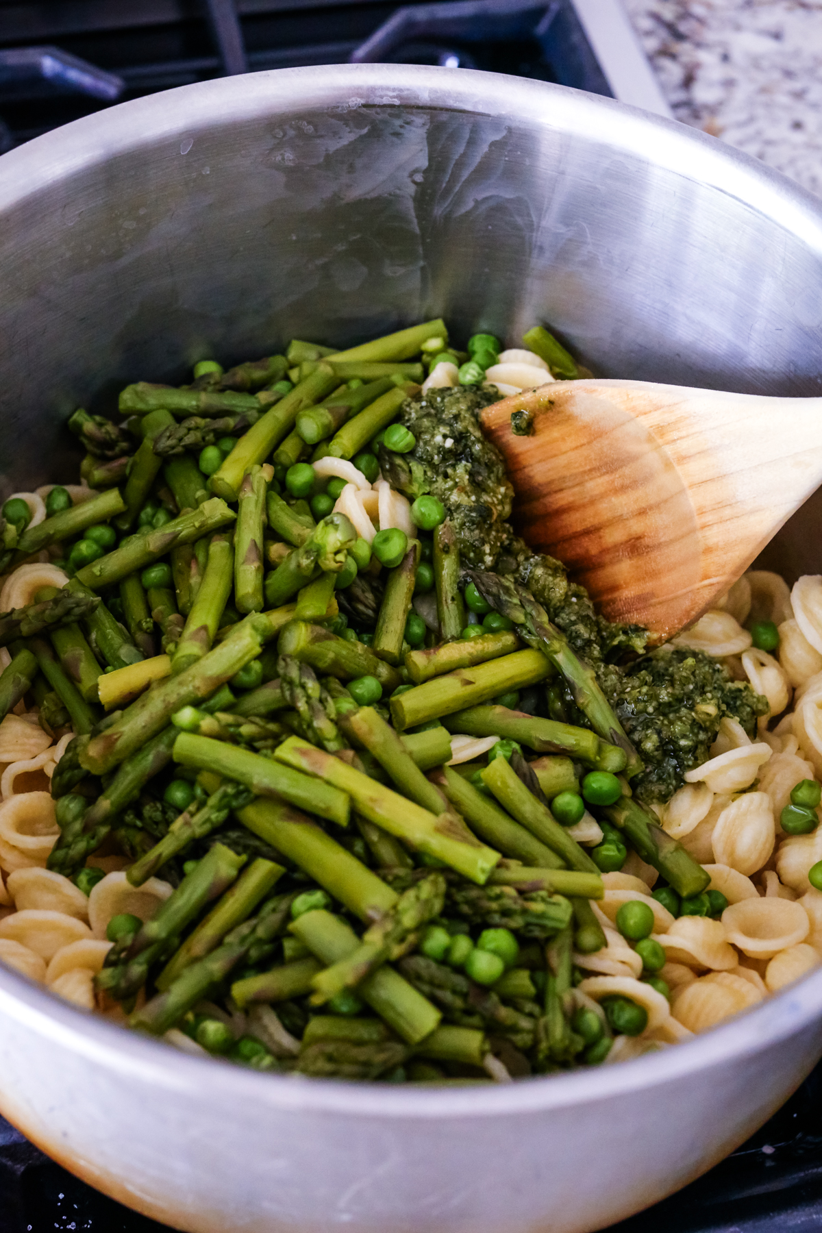 adding asparagus and peas to pasta and stirring them in