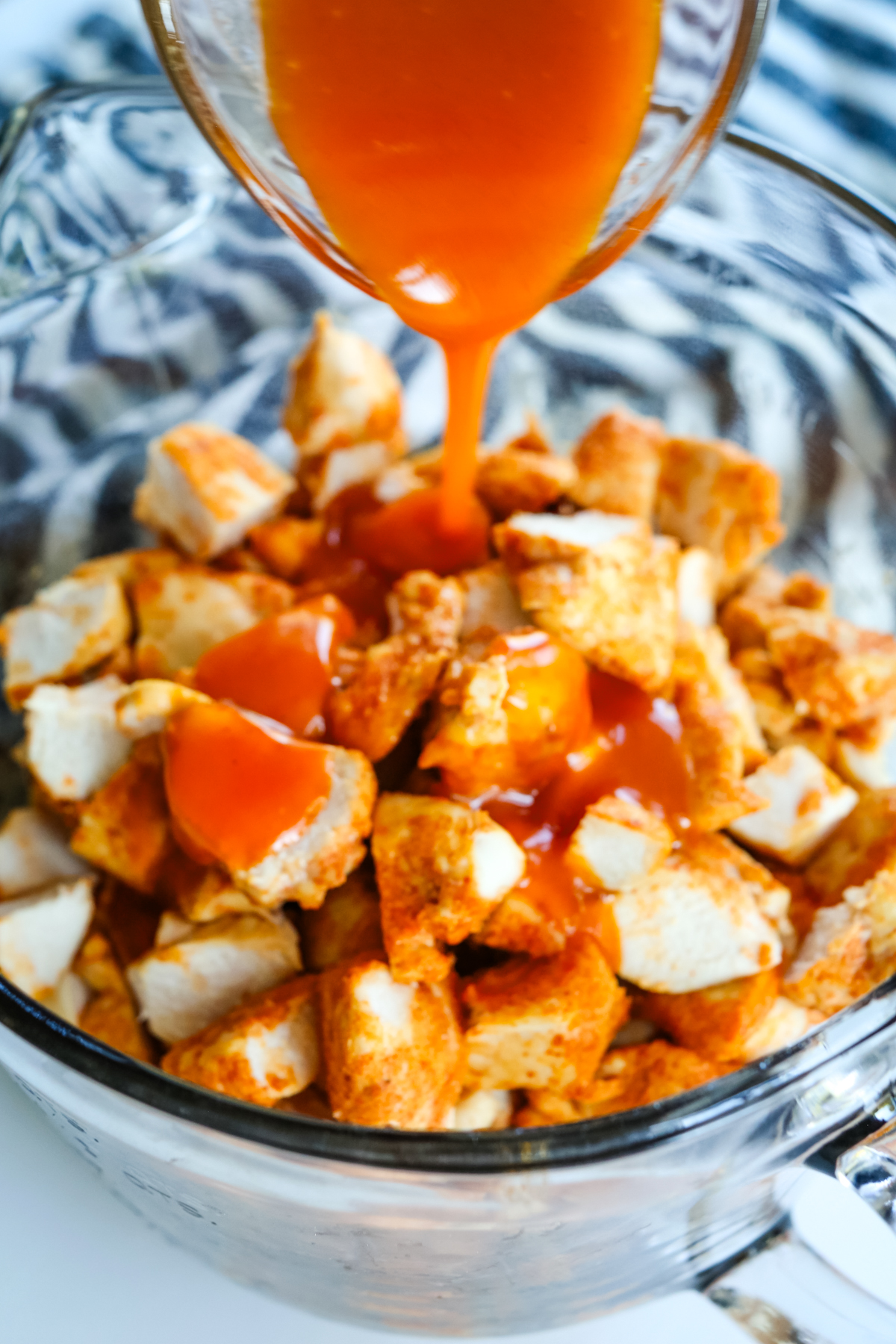 pouring buffalo sauce onto cooked chicken pieces 