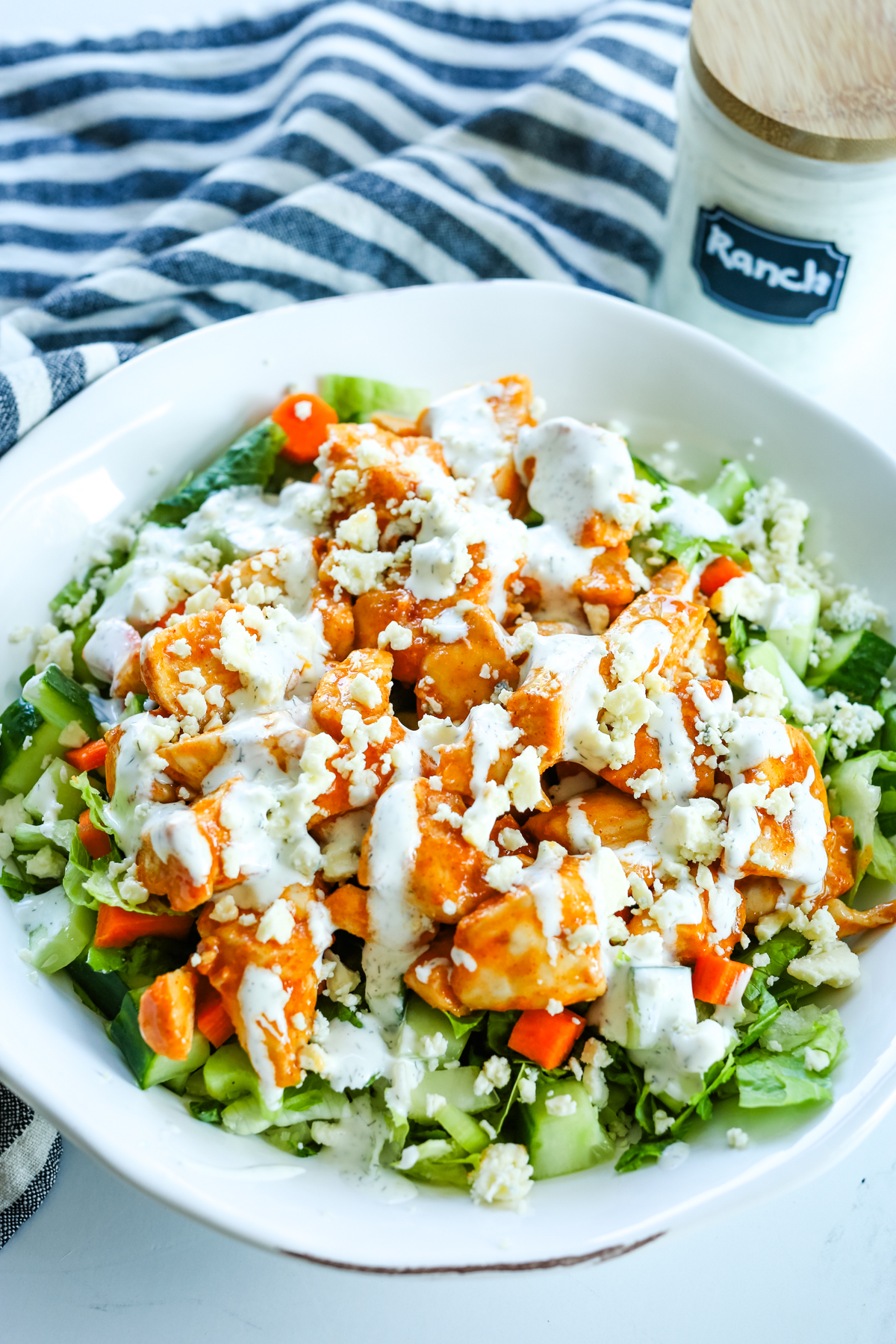 a white bowl with buffalo chicken salad and a striped napkin behind it