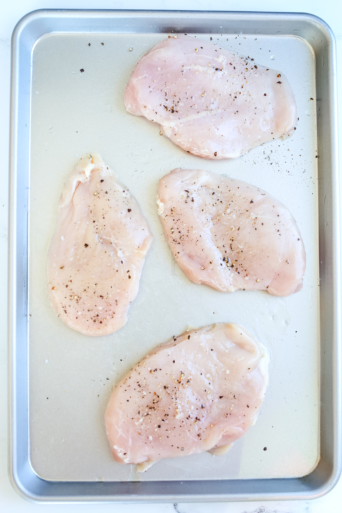 raw chicken breasts (seasoned) on a baking sheet