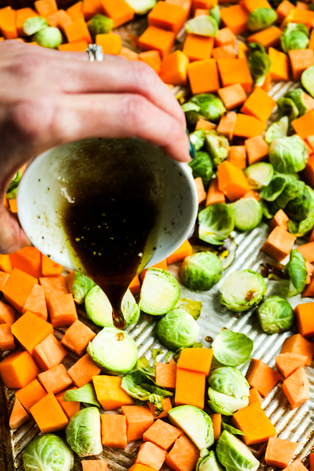 drizzling a brown liquid on a tray of cut vegetables 