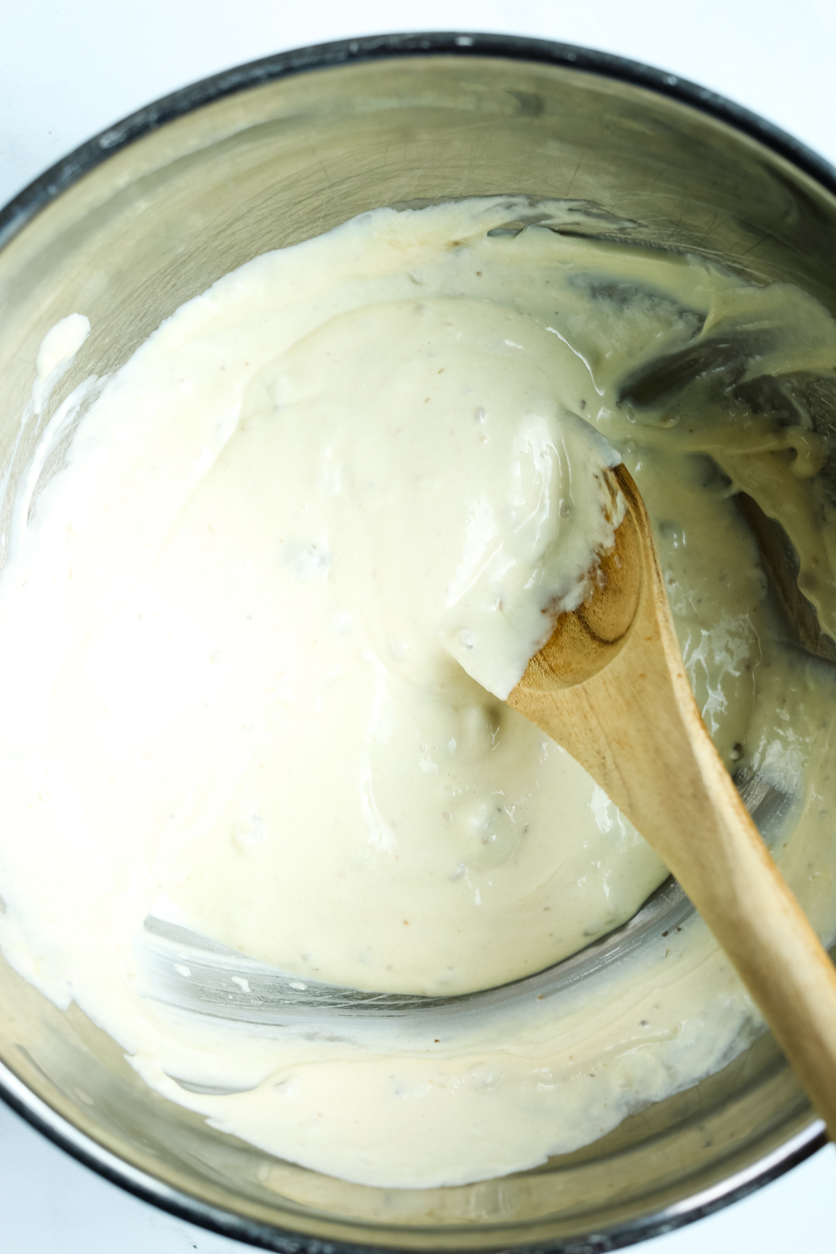 creamy looking mixture in a bowl being mixed with a wooden spoon