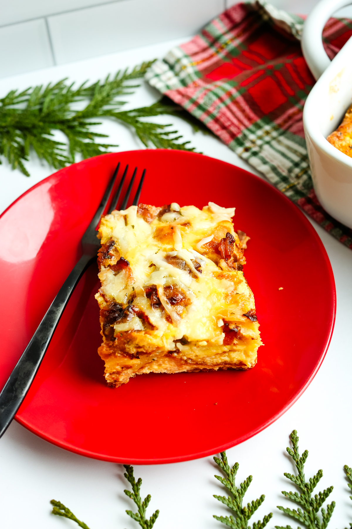 a square of casserole on a red plate with a black fork
