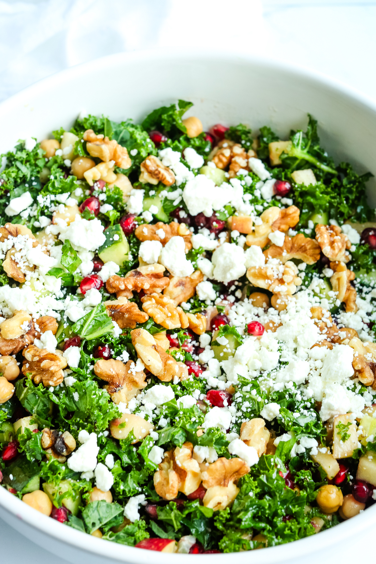 a large white bowl filled with kale, pomegranate seeds, walnuts, and goat cheese 