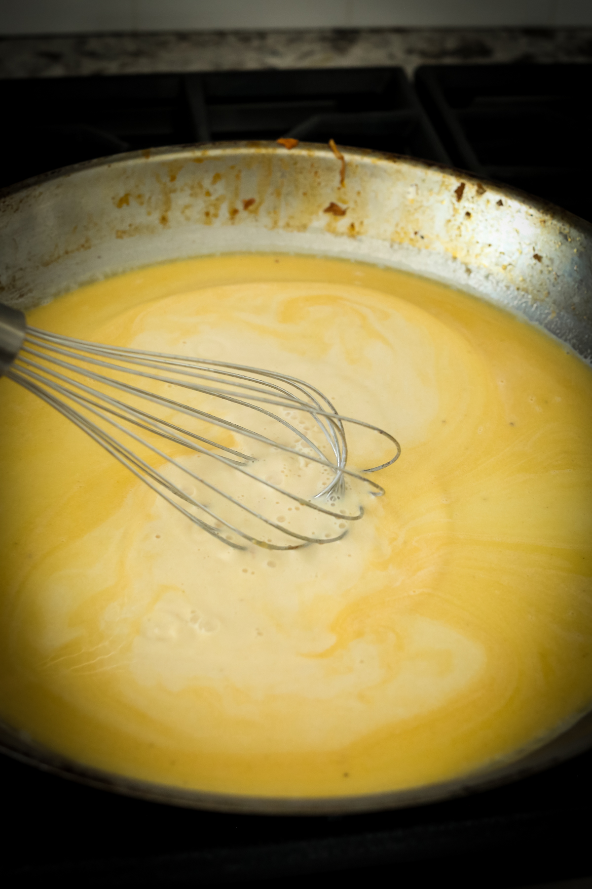 an orange hued sauce in a large skillet with a whisk