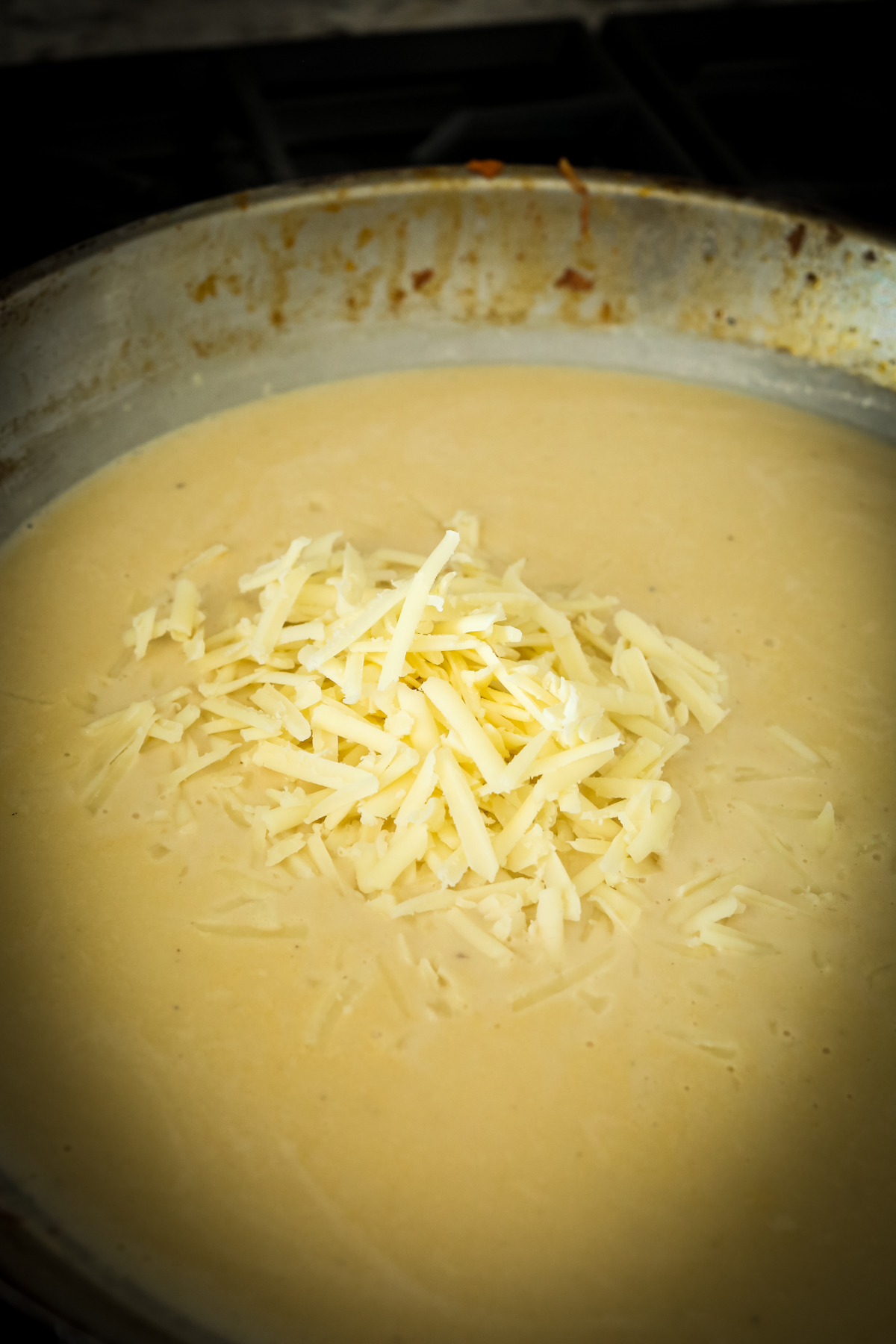 shredded cheese on top of an orange sauce in a large skillet