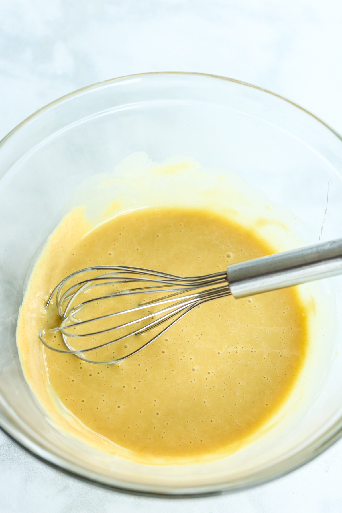 whisking together a yellow hued sauce in a glass bowl 