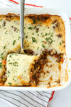 cottage pie in a casserole dish with a spoon taking a portion out