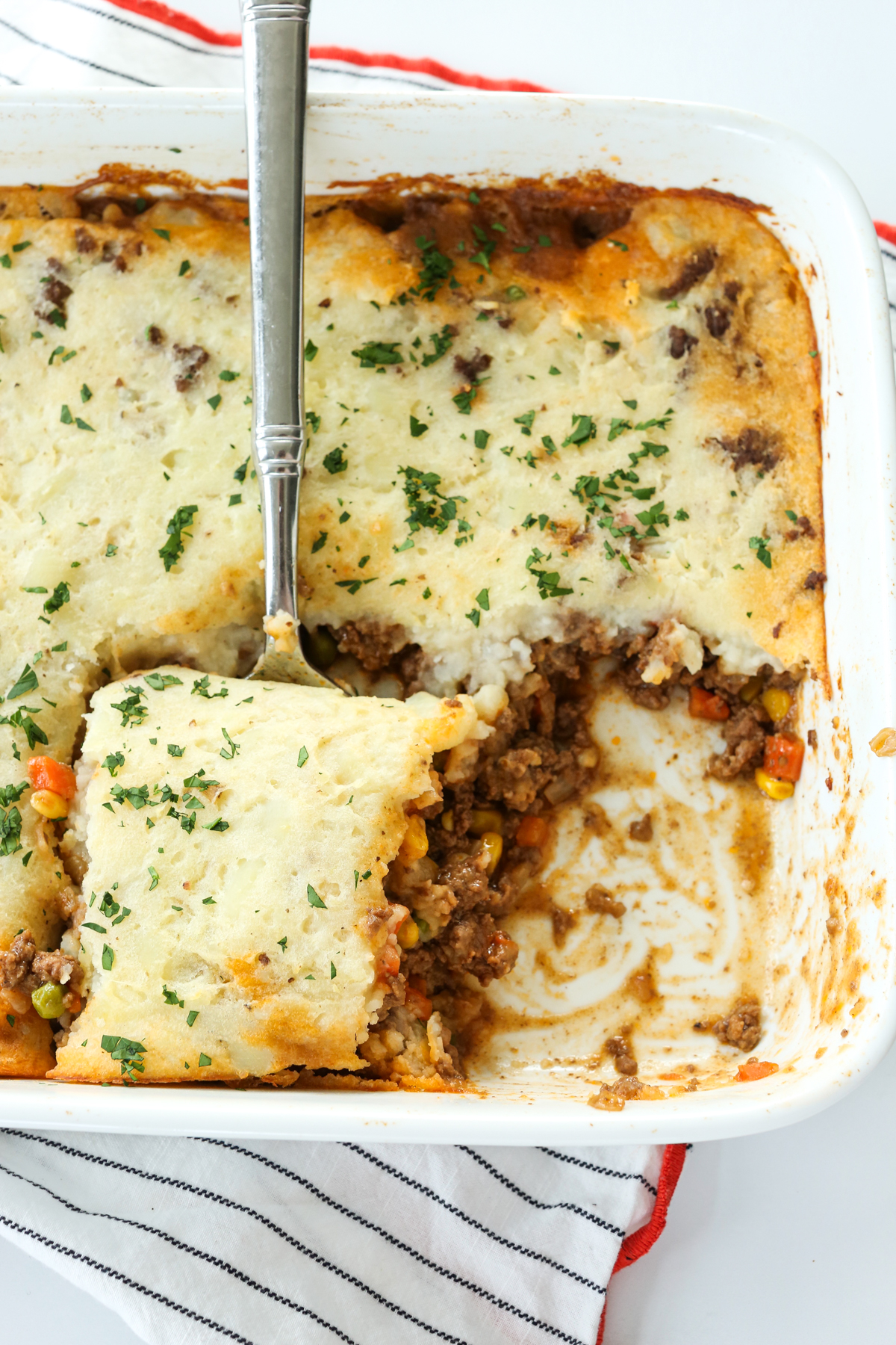 cottage pie in a casserole dish with a spoon taking a portion out
