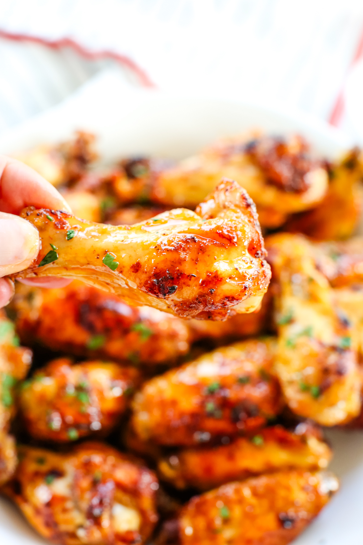 holding a chicken wing above a bowl of them