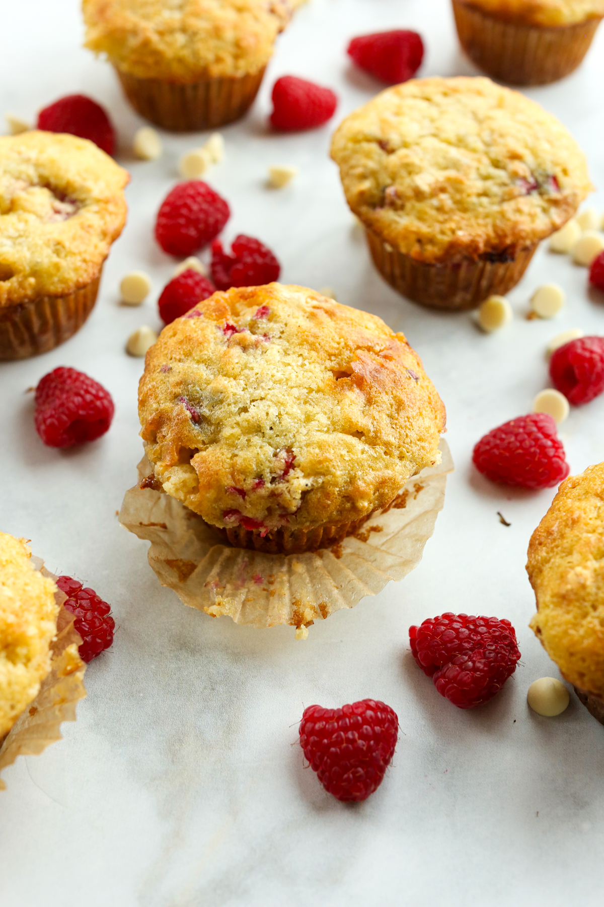 muffins on a counter surrounded by fresh raspberries and white chocolate chips