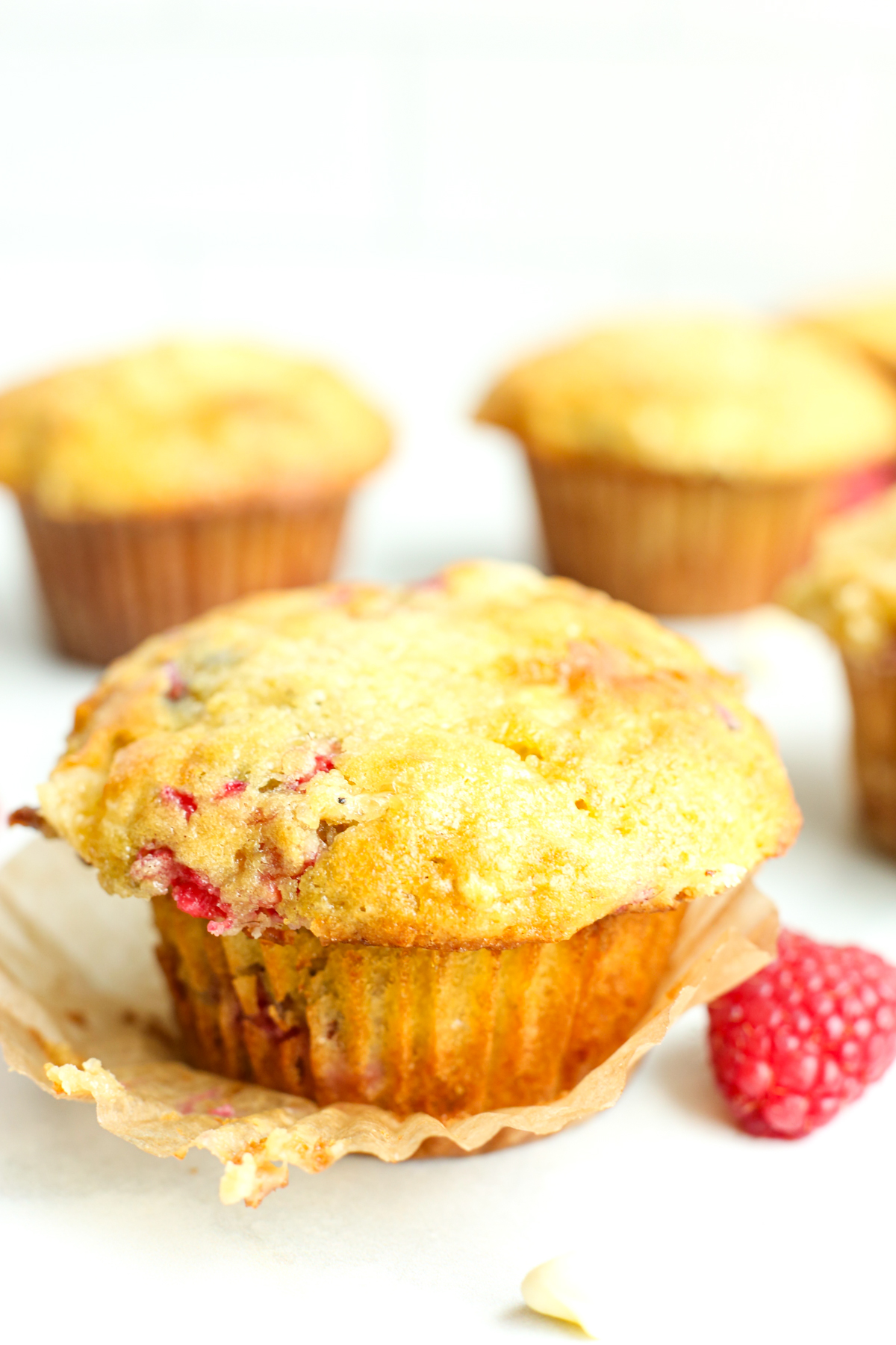 a Raspberry White Chocolate Muffin with the paper liner peeled off an a fresh raspberry next to it 
