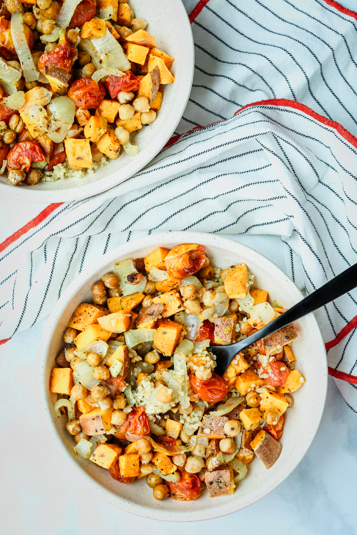 two bowls of roasted vegetable quinoa salad with a striped napkin between them