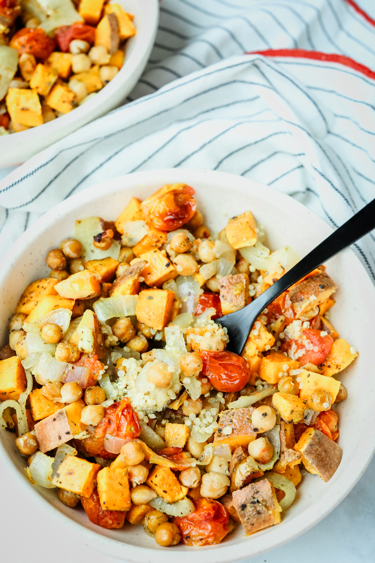 Overhead picture of roasted vegetable quinoa salad in a white bowl with a black fork